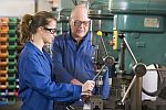 meisje aan het werk aan machine onder begeleiding van een oudere mannelijke werknemer