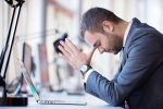 man zit met zijn handen gevouwen aan zijn bureel